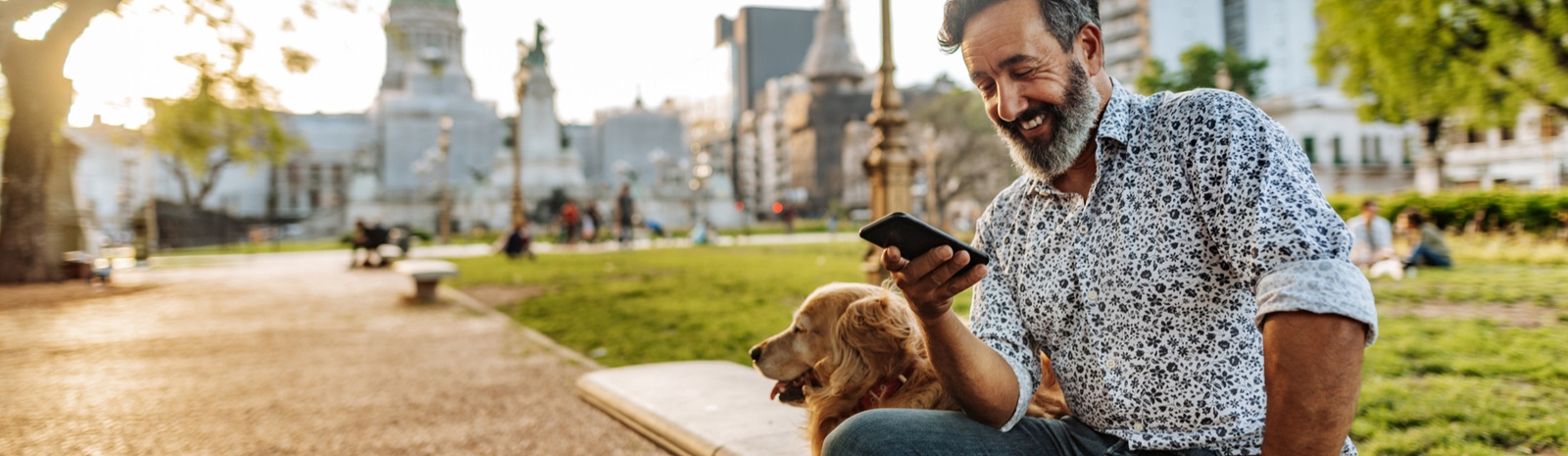 Man sitting outside with dog looking at cell phone